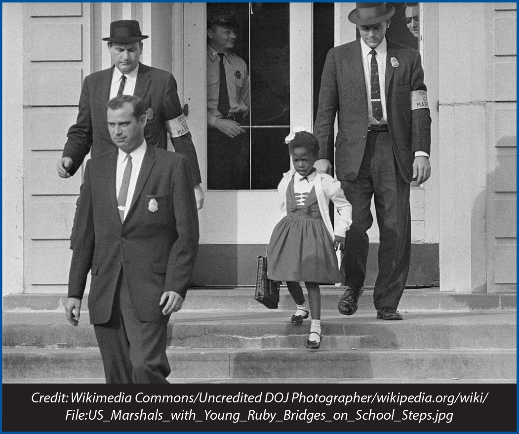 In November 1960, U.S. Deputy Marshals escort six-year-old Ruby Bridges from William Frantz Elementary School in New Orleans. | Credit: Wikimedia Commons/Uncredited DOJ Photographer